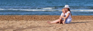 Genç anne oğluyla deniz plajında. Çocuk, sahil siting kız. Sarılma, gülümseyen, yaz günü, yaşam tarzı anne birlikte çocuk çocuk. Kum, okyanus arka plan. Panoramik, afiş, kopya alanı. Konsept tatil, tatil.