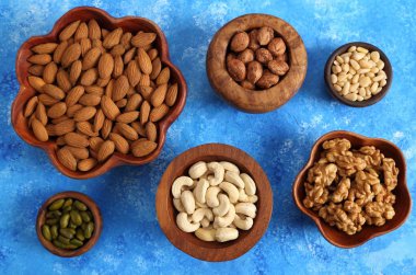 Mavi bir arka plan üzerinde ahşap kase fındık farklı türleri. Üstten görünüm.