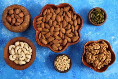 Mavi bir arka plan üzerinde ahşap kase fındık farklı türleri. Üstten görünüm.