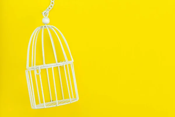 Protec olarak kullanarak düz sarı arka plan üzerinde küçük beyaz kuş kafesi — Stok fotoğraf
