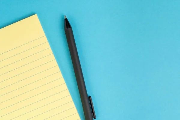 Bloc de notas de papel amarillo pequeño con página en blanco, pluma sobre ba azul sólido — Foto de Stock