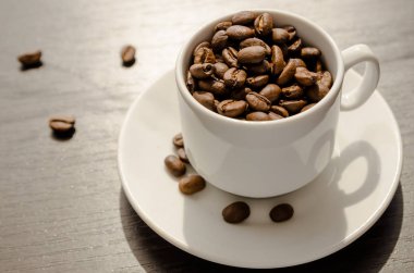 Fincan kahve çekirdekleri ile doldurulur. Kahve çekirdekleri masanın üzerine dağılmış.