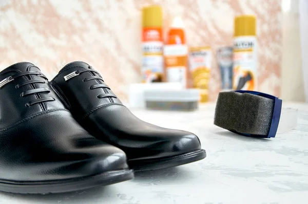 Men\'s, black, shiny shoes on a light surface. In the background are Shoe care accessories. Clean shoes.