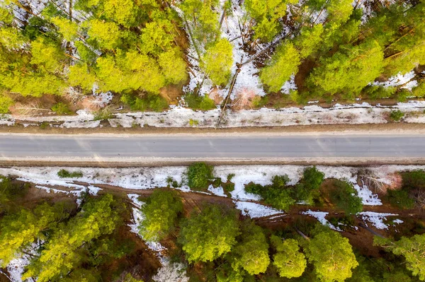 Weg in het voorjaarbos. Sneeuw smelt aan de zijkant van de weg en tussen de bomen. Luchtfoto van Drone — Stockfoto