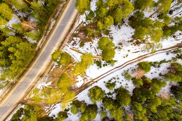 Weg in het voorjaarbos. Sneeuw smelt aan de zijkant van de weg en tussen de bomen. Luchtfoto van Drone — Stockfoto