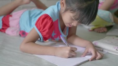 Asyalı çocukların küçük kızları evde ders çalışıyorlar ve bir deftere yazıyorlar..