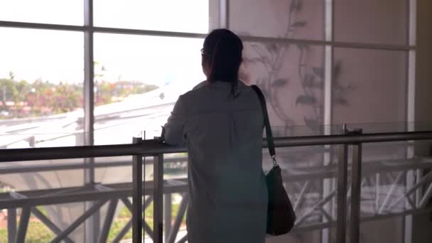 アジアの女性は空港の窓から外を見る — ストック動画