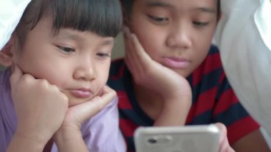 Asyalı çocukların erkek ve kız kardeşi battaniyenin altında tablet kullanıyor..