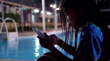 Asyalı çocuk akıllı telefon kullanıyor. Akşamları havuz kenarında dinleniyor..