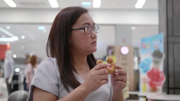亚洲女人 戴着眼镜坐在咖啡店里吃甜甜圈 — 图库视频影像