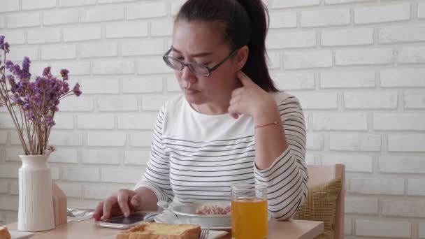 Asiatische Frau benutzt und berührt ein Smartphone, während sie in Caf frühstückt.