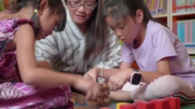 Mutlu Asya Aile, Genç Anne ve kızları ahşap blok kule inşa etmeye çalışın.