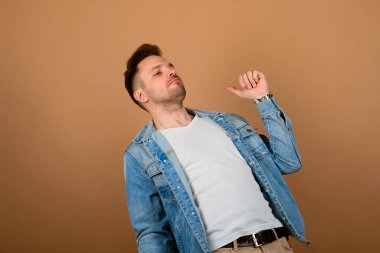 Yakışıklı adam ayakta ve gülümsüyor açık kahverengi stüdyo arka planında izole edilmiş. Yarım boy erkek portresi. İnsan duyguları, yüz ifadesi konsepti..