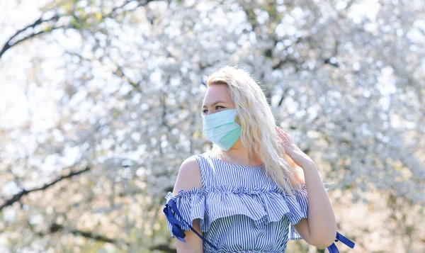 Uma menina em uma máscara médica protetora na primavera entre o jardim florescendo. .. Concepção de alergia primavera — Fotografia de Stock