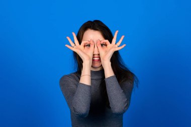 Gülümseyen, mavi arka planda gri elbiseli neşeli genç bir kadının fotoğrafı. Duygusal Portre