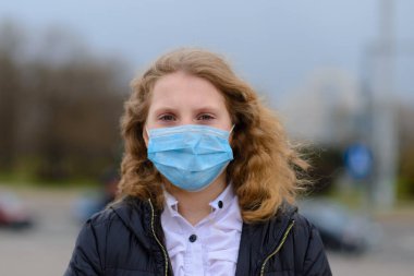 Kapalı oyun parkında yüzü maskeli, üzgün, beyaz bir çocuğun portresi. Coronavirus sosyal mesafesi ve karantina.