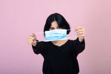 Mavi renkli koruyucu yüz maskesi takan beyaz kız. Pembe arka planda portre çekimi. Virüs ve kirliliği koruma kavramı.