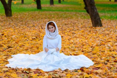 Uzun beyaz gelinlikli şirin kız kırsal yolda poz veriyor altın saatinde ormanda sonbahar ağaçları arasında..