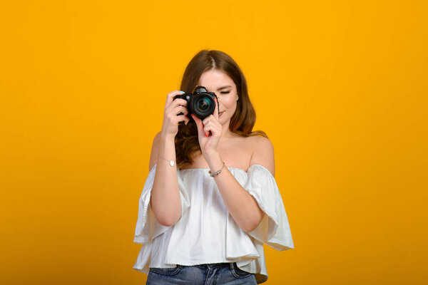 Young female photographer with camera over yellow background, smiling, happy.