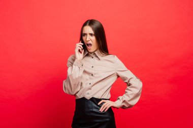 Şaşırmış genç bir kadın akıllı telefon kullanıyor, kırmızı arka plan.