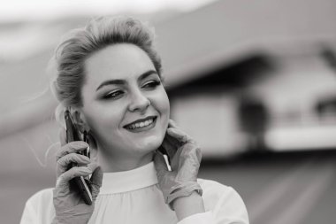 Telefonlu, defterli, tabletli, açık havada kahve içen genç bir iş kadınının portresi. Lastik mavi eldivenli güzel sarışın kız..