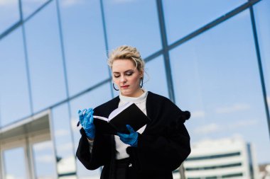 Telefonlu, defterli, tabletli, açık havada kahve içen genç bir iş kadınının portresi. Lastik mavi eldivenli güzel sarışın kız..