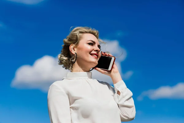 Portrait of a young businesswoman with phone, notebook, tablet, coffee outdoors. Pretty blonde girl in rubber blue gloves.