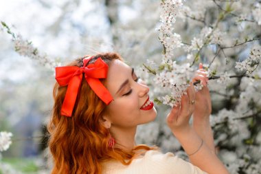 Bahar çiçekleri içinde beyaz elbiseli güzel kızıl saçlı genç kadının portresi.