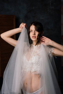 Beyaz iç çamaşırlı güzel gelin yatak odasında ve stüdyosunda oturuyor. Düğün konseptinin sabahı