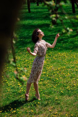 Yaz kenti parkında çimlerde oturan mutlu genç bir kadın. Açık havada.