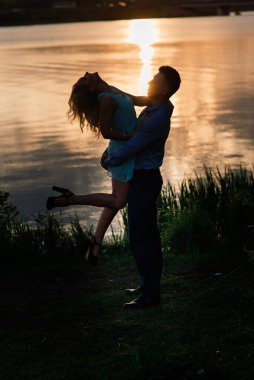Birbirine aşık çiftler, turuncu gün batımında gölün arkasında hafif bir siluet. Romantik..