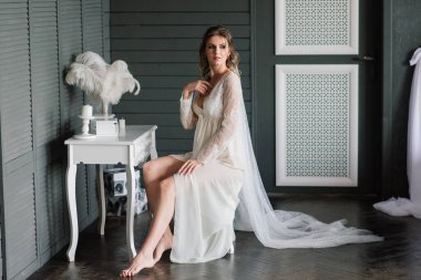 Beyaz dantelli iç çamaşırlı güzel bir gelin, bir otel odasında çıplak omuzlu, yatak odasında oturuyor. Mutlu düğün sabahları..