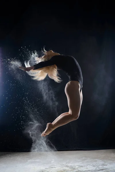 空飛ぶ白い粉の雲で覆われた黒い体操服を着て美しいふっくらブロンドの女の子は 暗闇の上に座って踊るジャンプします 芸術的な概念と広告写真 スペースのコピー — ストック写真