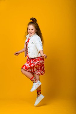 Mutlu kaygısız çocuk duyguları. Enerjik, neşeli, sevimli küçük kız stüdyoda sarı arka planda şakalara gülüyor..