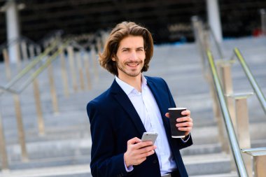 Yakışıklı bir işadamının portresi telefon ve kahve fincanı şehir sokaklarında.