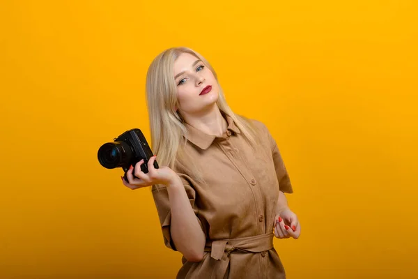 一个金发女郎的画像 她手里拿着相机 背景是黄色的 独立的工作室 摄影日 — 图库照片