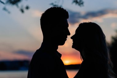 Birbirine aşık çiftler, turuncu gün batımında gölün arkasında hafif bir siluet. Romantik..