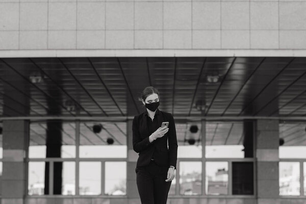 Красивая деловая женщина в черном костюме в черной медицинской маске и перчатках на город в карантине и изоляции. Пандемия COVID-19. Изображение с избирательным фокусом