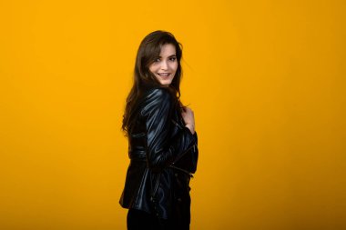 Heyecanlı genç esmer kadın ellerini kaldırırken bir şey hakkında seviniyor, sarı arka planda siyah elbiseler giyiyor.