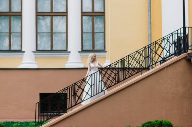 Parkta yürüyen ve gülümseyen kıvırcık saçlı sarışın gelin, konsept düğün.