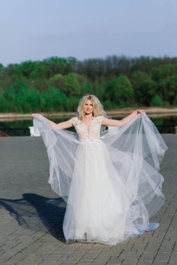 Parkta yürüyen ve gülümseyen kıvırcık saçlı sarışın gelin, konsept düğün.