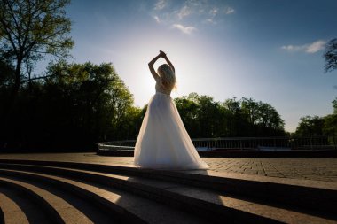 Parkta yürüyen ve gülümseyen kıvırcık saçlı sarışın gelin, konsept düğün.