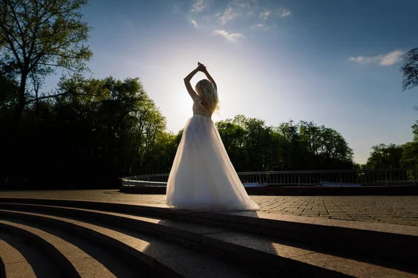 Parkta yürüyen ve gülümseyen kıvırcık saçlı sarışın gelin, konsept düğün.