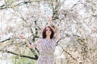 Bahar çiçekli bahçede poz veren kıvırcık saçlı çekici bir kadın.