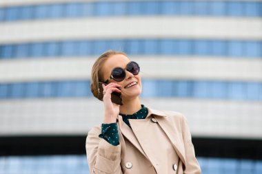 Güneş gözlüklü, telefonlu, laptoplu, sokaklarda kahve içen genç ve güzel bir iş kadını.