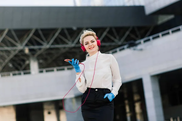 Portrait of a young businesswoman with phone, notebook, tablet, coffee outdoors. Pretty blonde girl in rubber blue gloves.