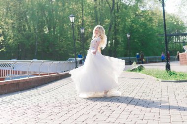 Parkta yürüyen ve gülümseyen kıvırcık saçlı sarışın gelin, konsept düğün.