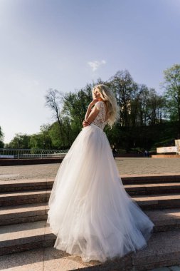 Parkta yürüyen ve gülümseyen kıvırcık saçlı sarışın gelin, konsept düğün.