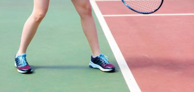 Tenis kortunda raketle genç bir kızın bacakları.