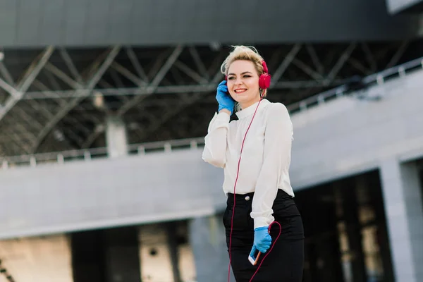 Portrait of a young businesswoman with phone, notebook, tablet, coffee outdoors. Pretty blonde girl in rubber blue gloves.